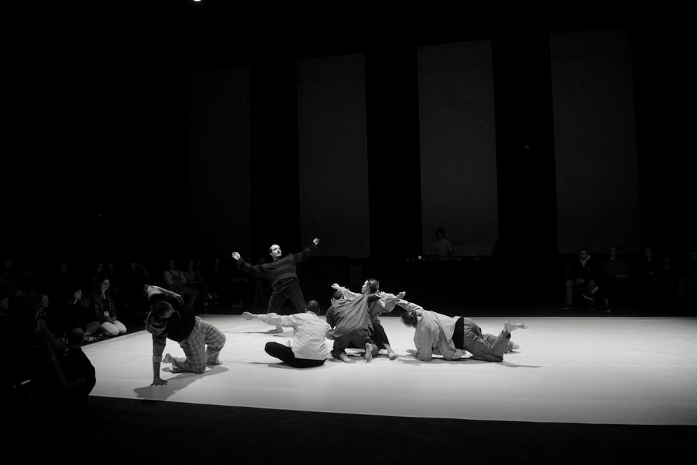 fotografia czarno biała przedstawiająca grupę sześciorga tancerzy na scenie i publiczność z pierwszego rzędu